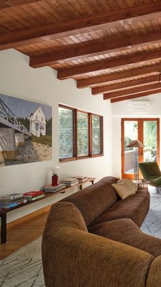 a living room filled with furniture and lots of wood beams on the ceiling, along with large windows