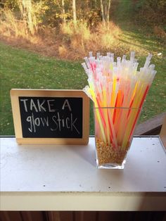 a glass vase filled with lots of different colored straws next to a sign that says take a glow stick