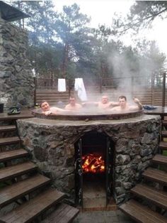 three people in a stone hot tub with wood steps leading up to the fire place