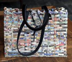 a handbag made out of newspapers sitting on top of a wooden table with a black handle