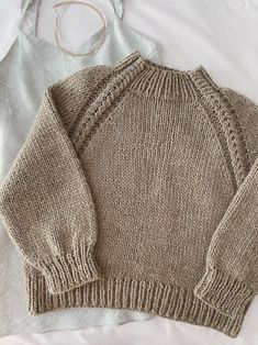 two sweaters laying on top of a bed next to a white bag and headband