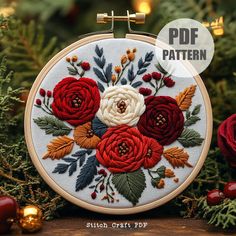 an embroidery pattern with red and white flowers on it, surrounded by greenery in front of a christmas tree