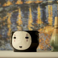 a black and white cup sitting on top of a table next to a green vase