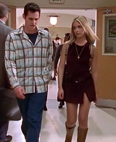 the young man and woman are walking down the hallway in front of other people wearing boots