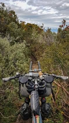 a bike parked on the side of a dirt road near some bushes and trees with clouds in the background