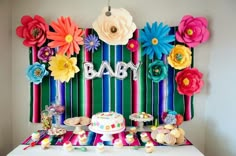 a baby shower party with colorful paper flowers on the wall and desserts on the table