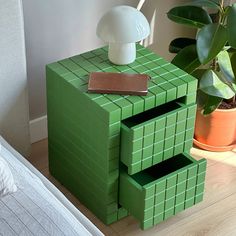 a green cube table with a lamp on top and a plant in the corner next to it