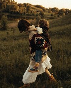 two children are walking through the grass in an open field, carrying each other on their back