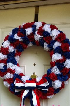 a wreath with red, white and blue flowers is hanging on the front door of a house