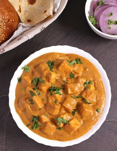 a white bowl filled with curry next to some bread and onion wedges on a table