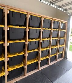 several storage bins with yellow handles are lined up against a wall in a garage