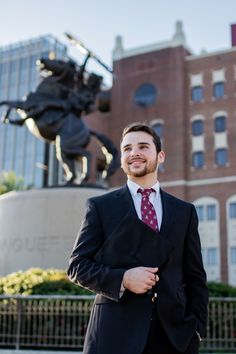 a man wearing a suit and tie standing in front of a building with a statue