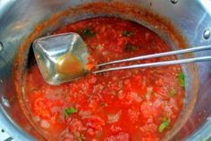 a large pot filled with lots of red sauce and some silver spoons in it