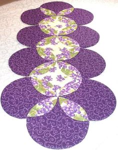 four purple and white placemats with green leaves on them, sitting on a bed