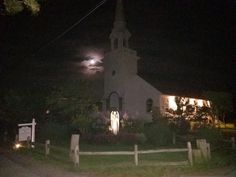 an old church lit up at night with the moon in the sky and lights on