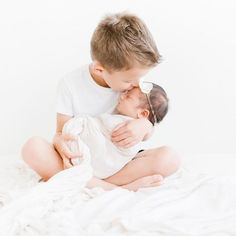 a young boy is kissing his baby on the bed