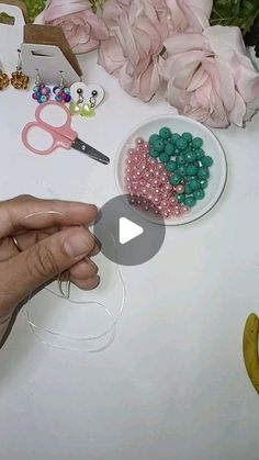 a person is making beads with scissors on a table next to flowers and pink roses