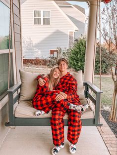 two people sitting on a porch swing wearing matching plaid pajamas and smiling at the camera