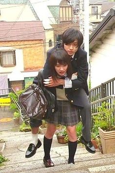 two young people are hugging each other on the steps in front of some houses and buildings