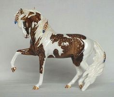 a figurine of a brown and white horse on a gray background with blue eyes