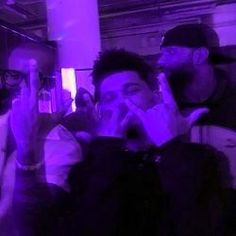 two men are talking on their cell phones in a room with purple lighting and one man is holding his hand up to his mouth