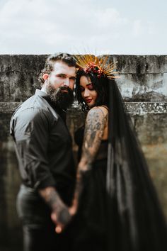 a man and woman standing next to each other in front of a wall with graffiti on it