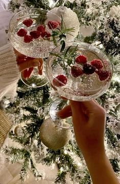 two wine glasses filled with raspberries sitting on top of a table next to a christmas tree