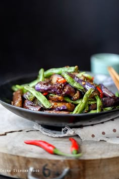 a black bowl filled with stir fry vegetables on top of a wooden table next to chopsticks