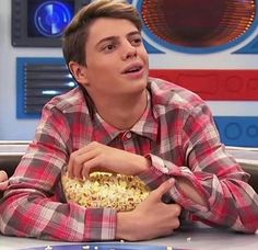 a young man sitting at a table with a bowl of popcorn in front of him