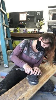 a woman sitting on top of a wooden bench wearing a mask and holding a shoe