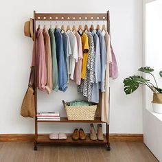 a rack with clothes hanging on it next to a potted plant