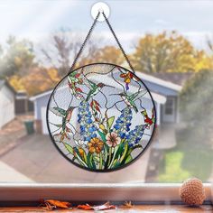 a round stained glass window with flowers hanging from it's side, in front of a house