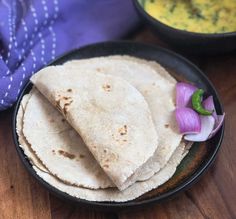 three tortillas on a black plate with purple onions