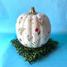 a white painted pumpkin sitting on top of some green leaves and grass with a blue background