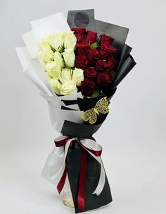 a bouquet of white and red roses wrapped in black paper