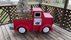 a red toy truck sitting on top of a wooden deck next to a christmas tree