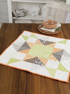 a wooden table topped with a green and orange quilt