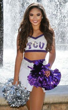 a cheerleader standing in front of a fountain with her pom - poms