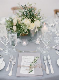 the table is set with white flowers and silverware