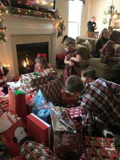 children opening christmas presents in front of the fire place with gifts piled on the floor