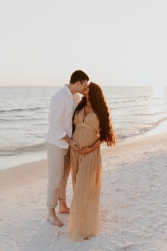 a pregnant couple kissing on the beach at sunset