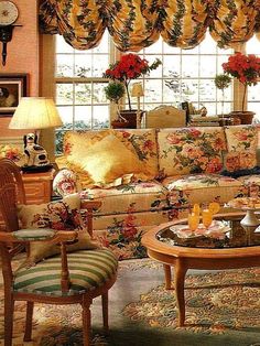 a living room filled with lots of furniture and flowers on the couches in front of large windows