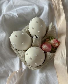 four eggs in a carton on a bed with a pink rose next to it