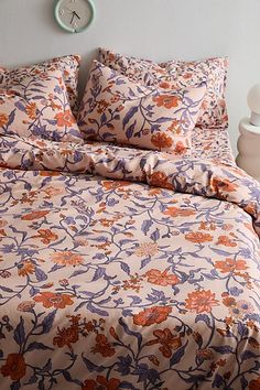 an orange and purple flowered comforter on a bed with two nightstands in the background