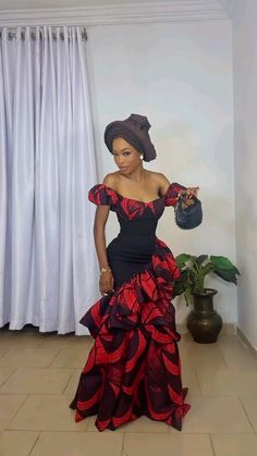 a woman in a black and red dress standing on the floor next to a potted plant