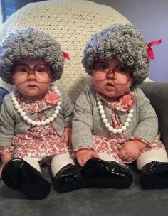 two baby dolls sitting on top of a gray couch next to each other wearing glasses