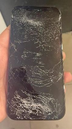 a hand holding a cell phone with cracked glass on the front and back cover,