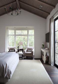 a large bedroom with two chairs and a bed in front of a window that looks out onto the woods