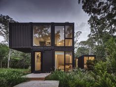 a house made out of shipping containers in the middle of some trees and grass with stairs leading up to it