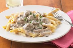 a white plate topped with pasta covered in meatballs and gravy next to a glass of water